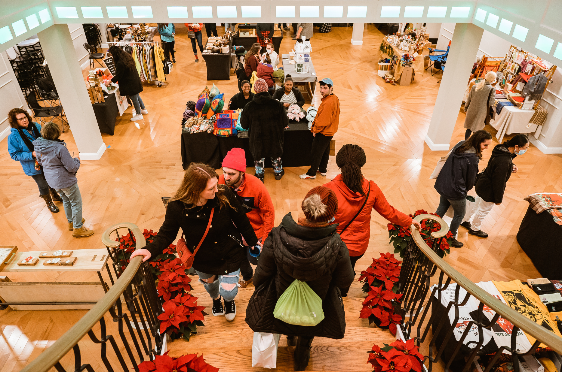 Holiday shoppers explore an indoor market set in a ballroom.