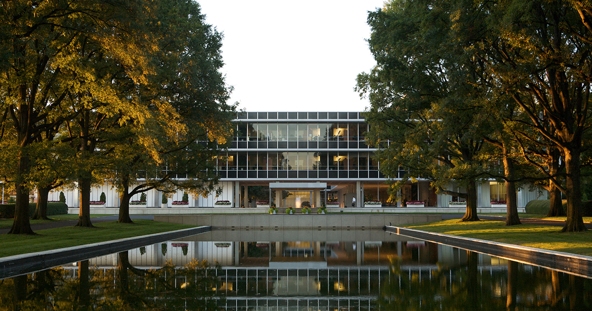 Glass building with reflecting pool and trees in golden light