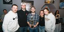 Five people stand in a row, with the person at center holding a trivia trophy.