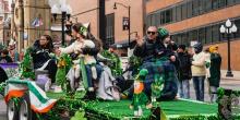 Family sits on green St. Patrick's Day parade float and waves at crowd