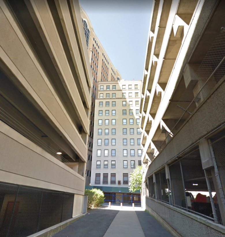 Narrow view down a side street, multi-level parking garages on either side of the street 