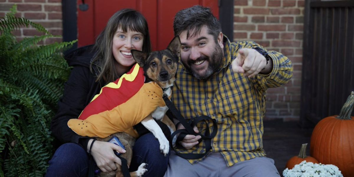 Two people hold dog and man on right points at camera