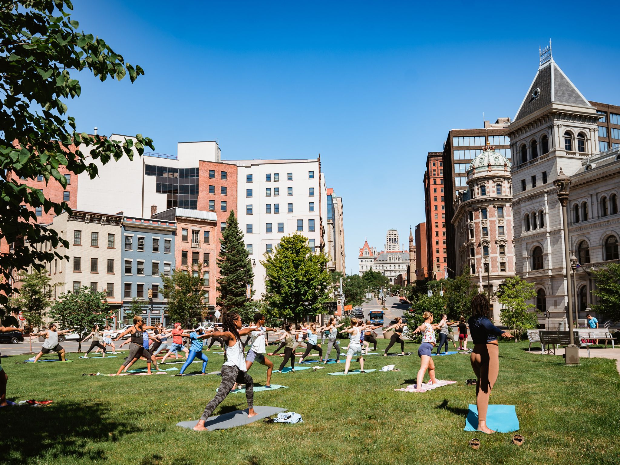 People in foreground doing yoga on lawn with city buildings in background