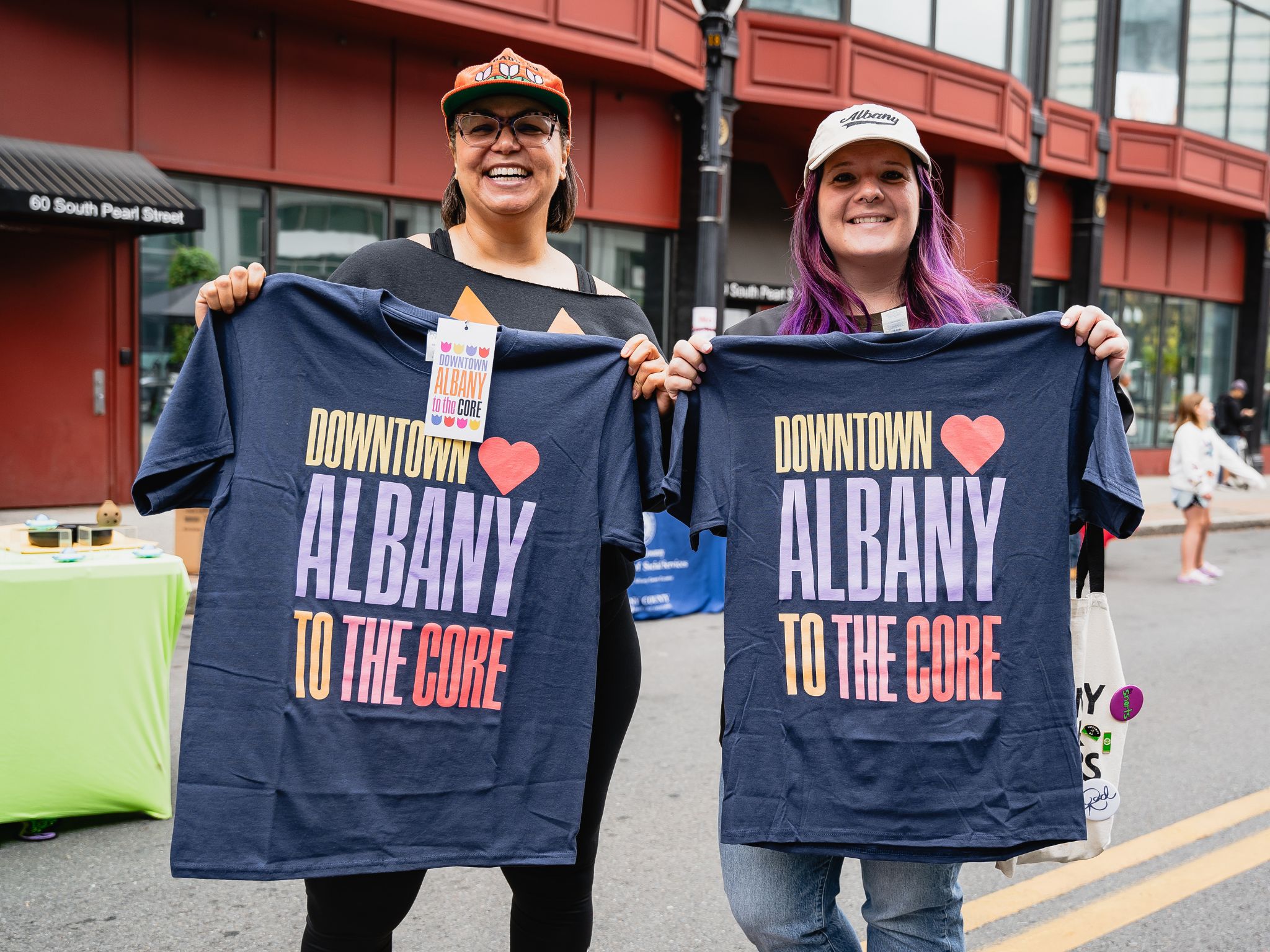 Two women stand in street holding t-shirts that read Downtown Albany to the Core