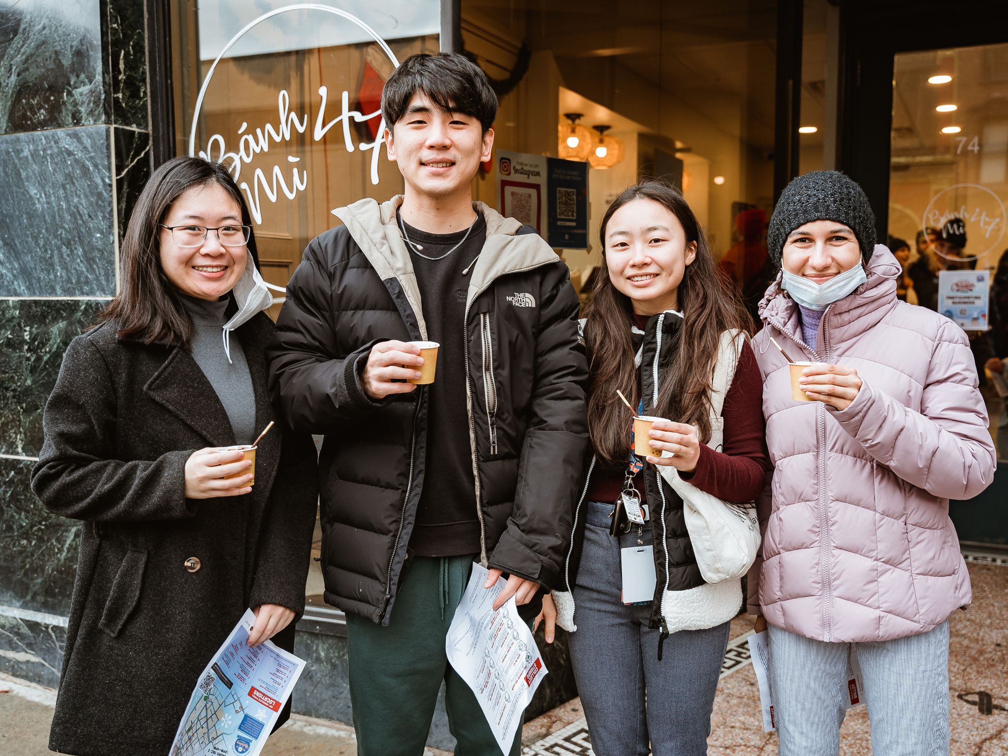 Four people stand in line holding cups of hot chocolate