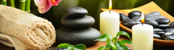 Towel, lit candles and smooth rocks in Asian wooden bowl