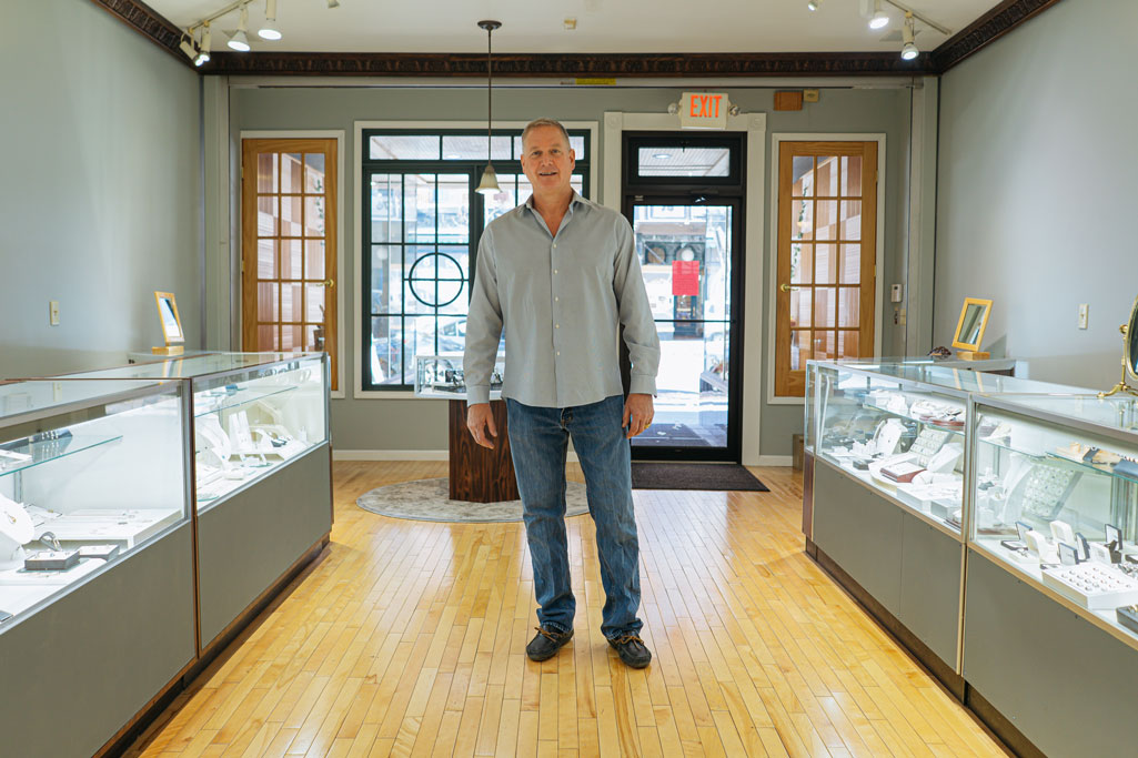 Truman Jewelers owner stands in the front of the store, jewelry cases on either side of him 