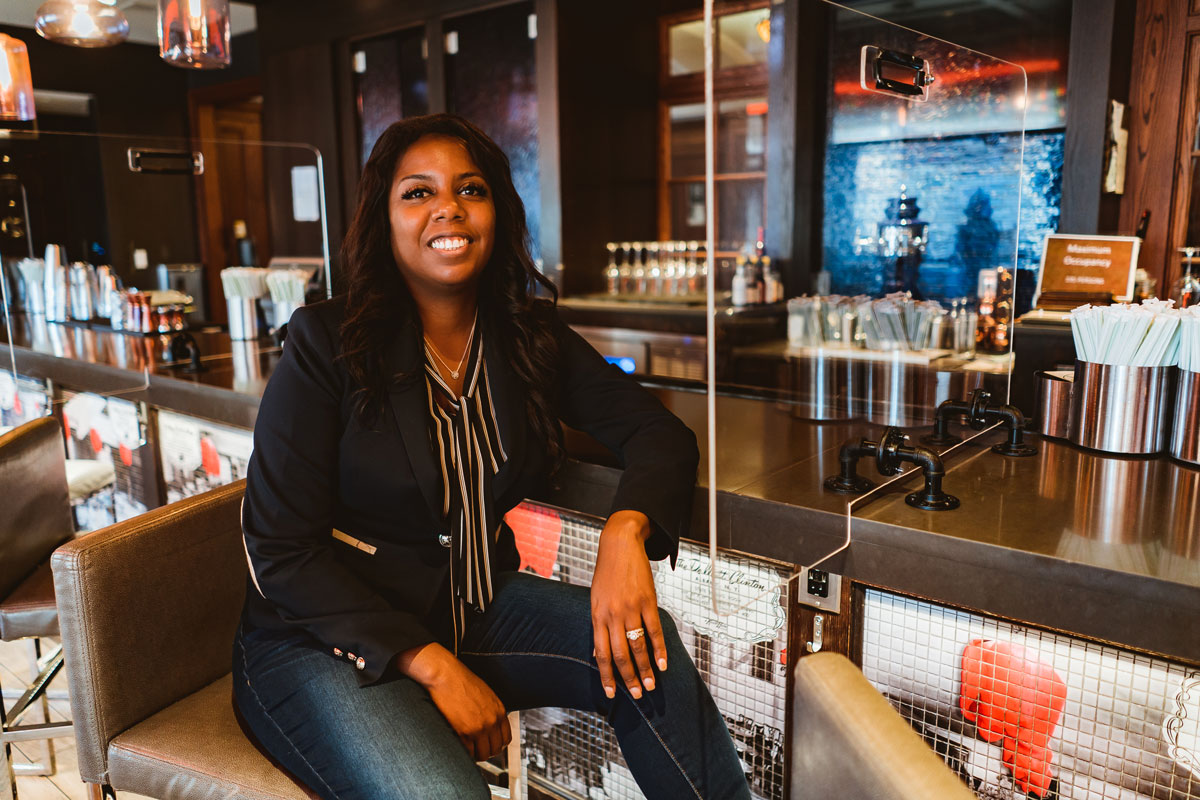 Business owner sits at her bar, smiling at the camera