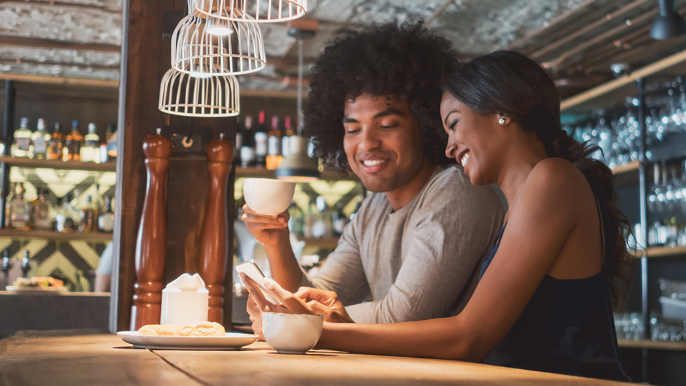 Young urban couple having coffee and using phone app