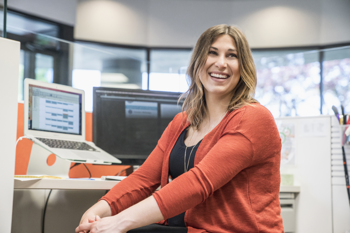 Young, smiling woman in cubicle with computer monitors