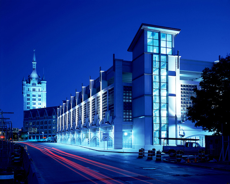 Night photo of glass and metal building lit up with Albany SUNY Admin building in background