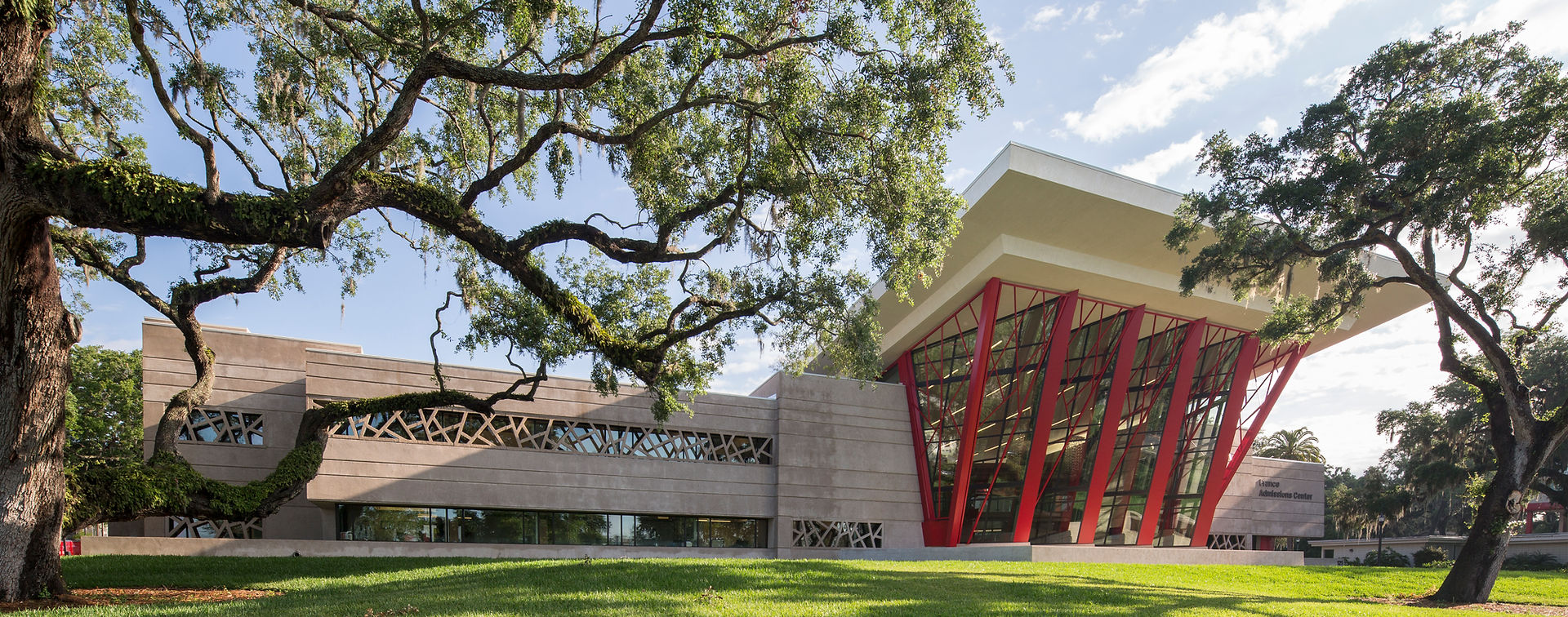 Dynamic image of a striking architectural building with angled red columns holding up a pergola in the front, patterned glass lining the facade. 