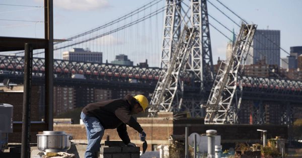 Masonry worker with hard hat and trowel in front of bridge and cityscape