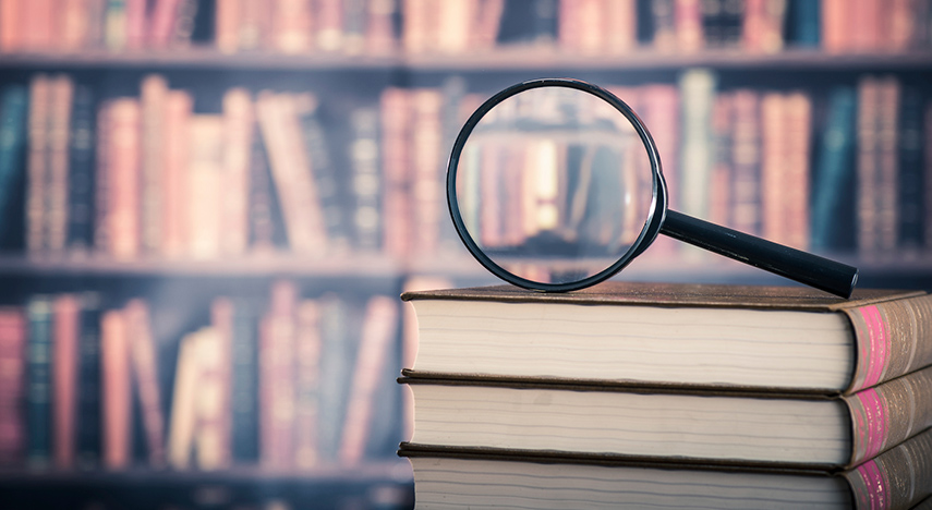 Magnifying glass on stack of books with law books on shelves in background