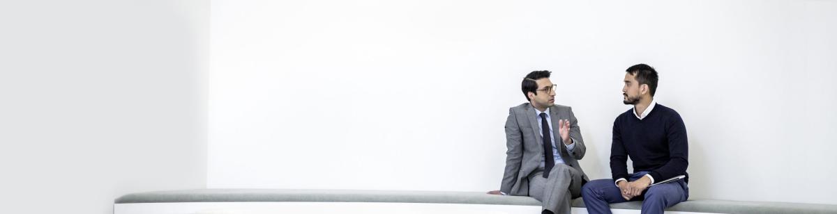 Man in business suit, talking to young man in front of white wall