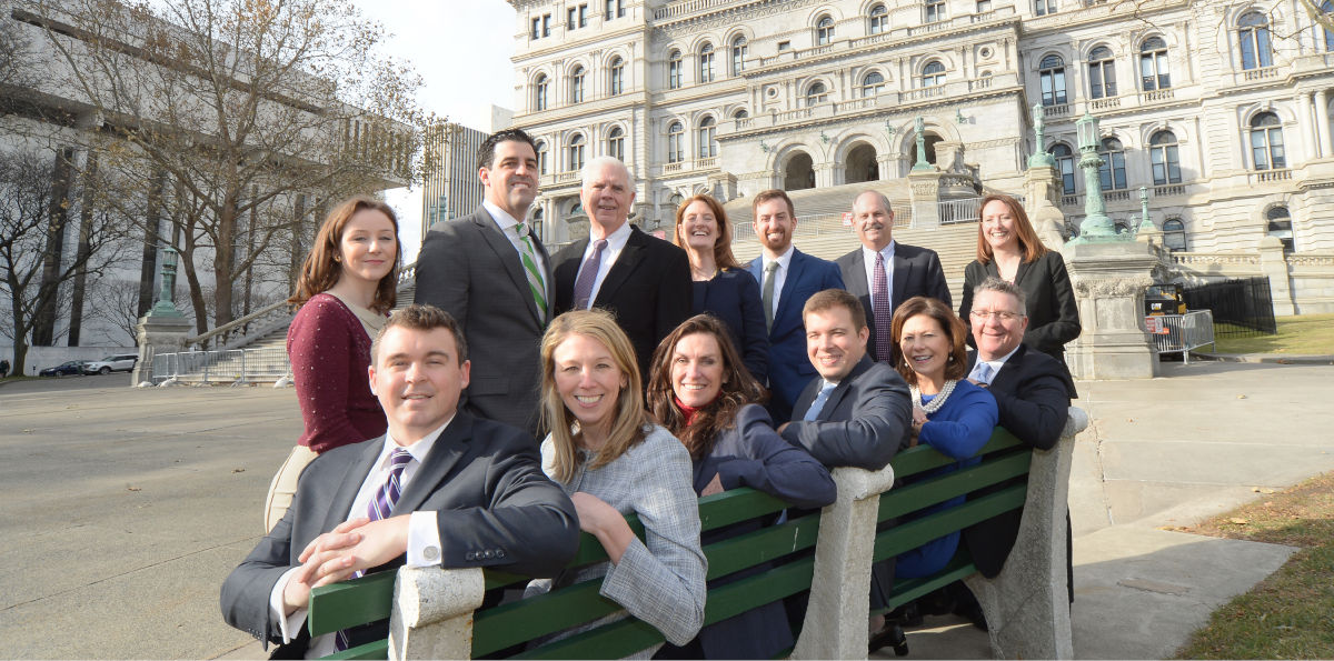Law firm staff gathered around bench near Capitol building in Albany