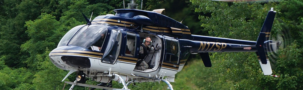 NYS helicopter with Trooper looking down at tree tops