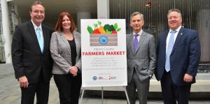 Poster at center with details of Albany County Farmers Market; two people stand on either side of poster