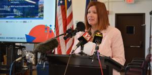 Woman stands at podium speaking into microphones in front of her 