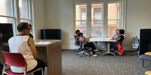 People at foreground and background sit at tables in office space