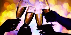 Four silhouetted hands hold champagne flutes in a toast