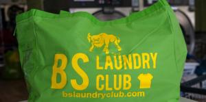 Image of green bag with yellow lettering reading "BS Laundry Club bslaundryclub.com" with bull and t-shirt icons also on bag