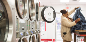 Dryers inside laundromat shown at left, with woman holding up piece of clothing on table at right