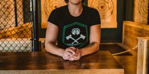 Owner of The Yard stands at a high top table in front of two axe throwing targets hung in the distance 