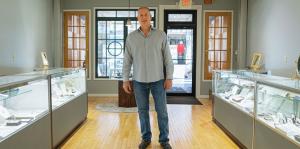 Truman Jewelers owner stands in the front of the store, jewelry cases on either side of him 