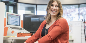 Young, smiling woman in cubicle with computer monitors