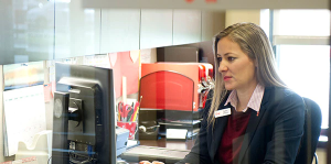 Woman on computer sitting behind glass partition with Key logo and Personal Banker sign