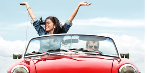 Woman with outstretched arms in red convertible, man at the wheel