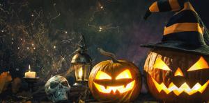Stock photo of spooky halloween jack-o-lanters wearing witch hats, a skull and candles on the left side of the image and the background is dark with spiderwebs 