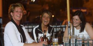 A candid photograph of three women out for drinks, smiling and laughing at the camera and at each other. 