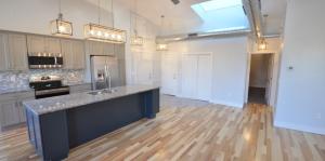 Kitchen view with island sink, cupboards, appliances, and view of other doors