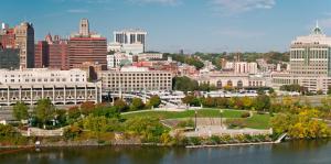 Aerial view of the Corning Preserve and buildings in Downtown Albany with the Hudson River in the foreground. 