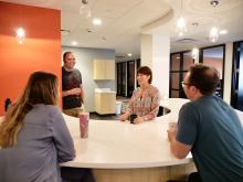 4 colleagues have a light hearted discussion while seated around a table.