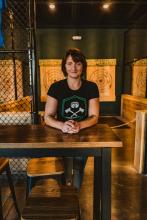 Owner of The Yard stands at a high top table in front of two axe throwing targets hung in the distance 