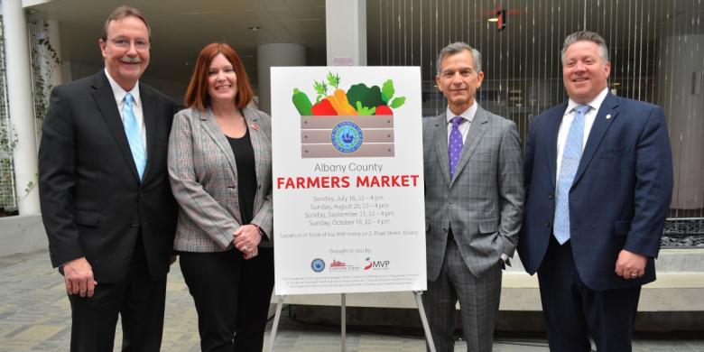 Poster at center with details of Albany County Farmers Market; two people stand on either side of poster