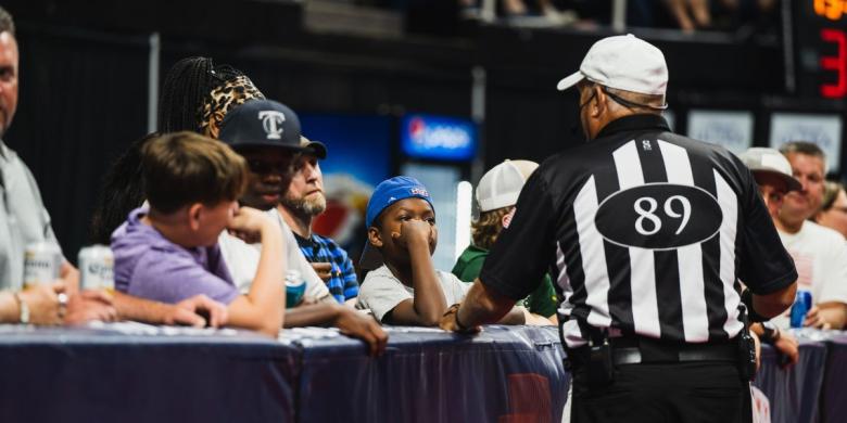 Adults and kids stand behind barrier while talking to referee, whose back is toward camera