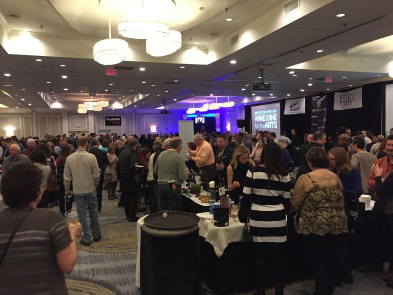 A crowd of patrons at the albany wine and dine for the arts event, networking and holding conversation over food and drink. 