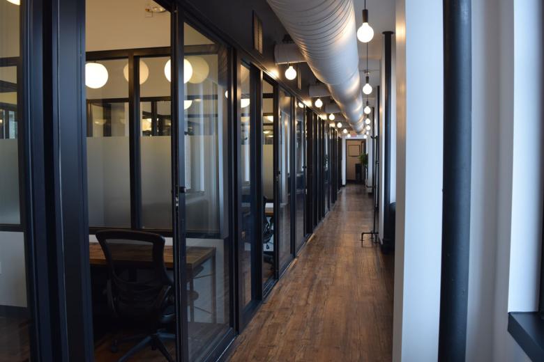 View down a newly renovated hallway, with big lightbulbs and many offices separated by glass 