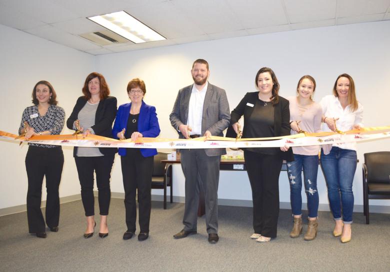 Employees stand with Albany Mayor and BID representatives holding a ribbon for their ribbon cutting ceremony