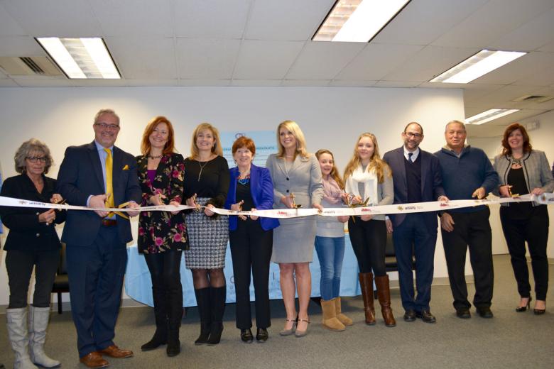 Employees stand with Albany Mayor and BID representatives holding a ribbon for their ribbon cutting ceremony