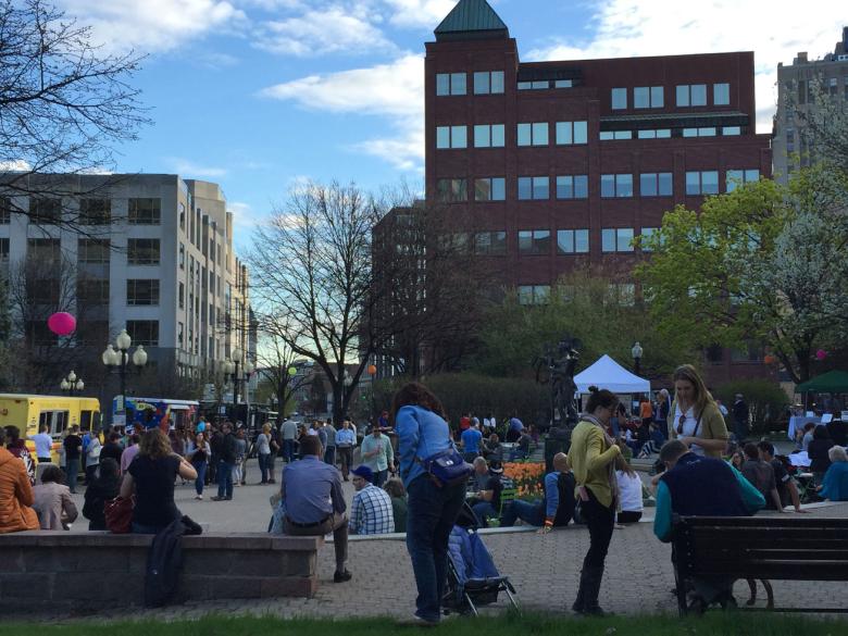 Crowd gathered outside, enjoying foods from various food trucks parked along the street on the left side of the image. 