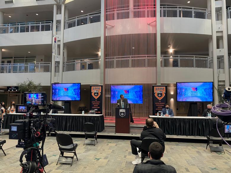 Press event with three screens, a few long tables, and a tv camera