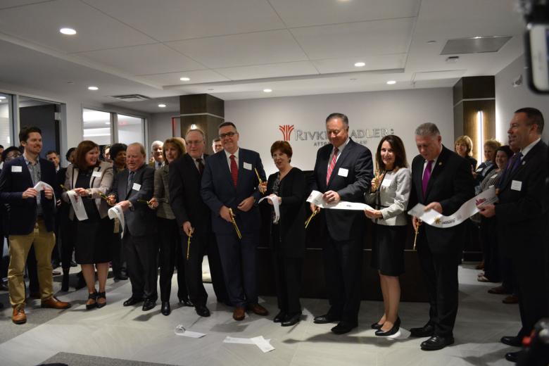 Employees stand with Albany Mayor and BID representatives holding a ribbon for their ribbon cutting ceremony