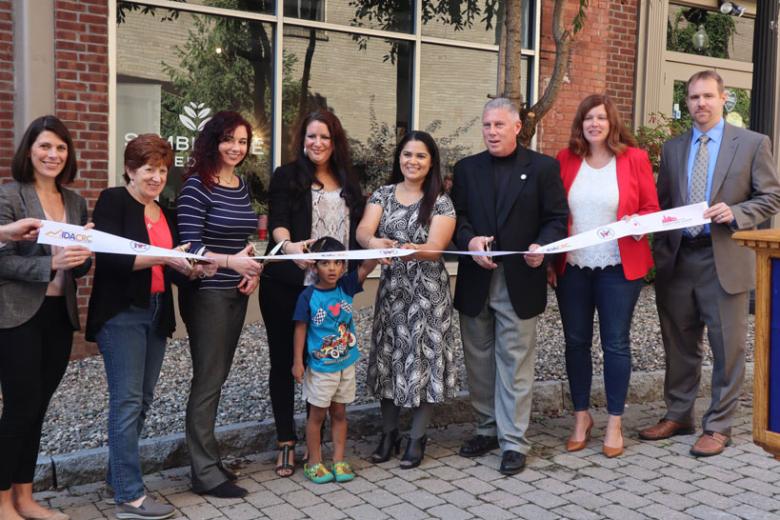 Employees stand with Albany Mayor and BID representatives holding a ribbon for their ribbon cutting ceremony