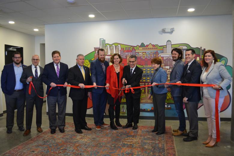 Employees stand with Albany Mayor and BID representatives holding a ribbon for their ribbon cutting ceremony