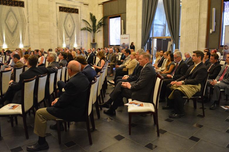 Aisle view of a packed room with rows of chairs filled with business people attending a meeting